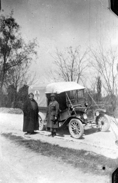 An old photograph of people in front of an antique car in the winter snow.