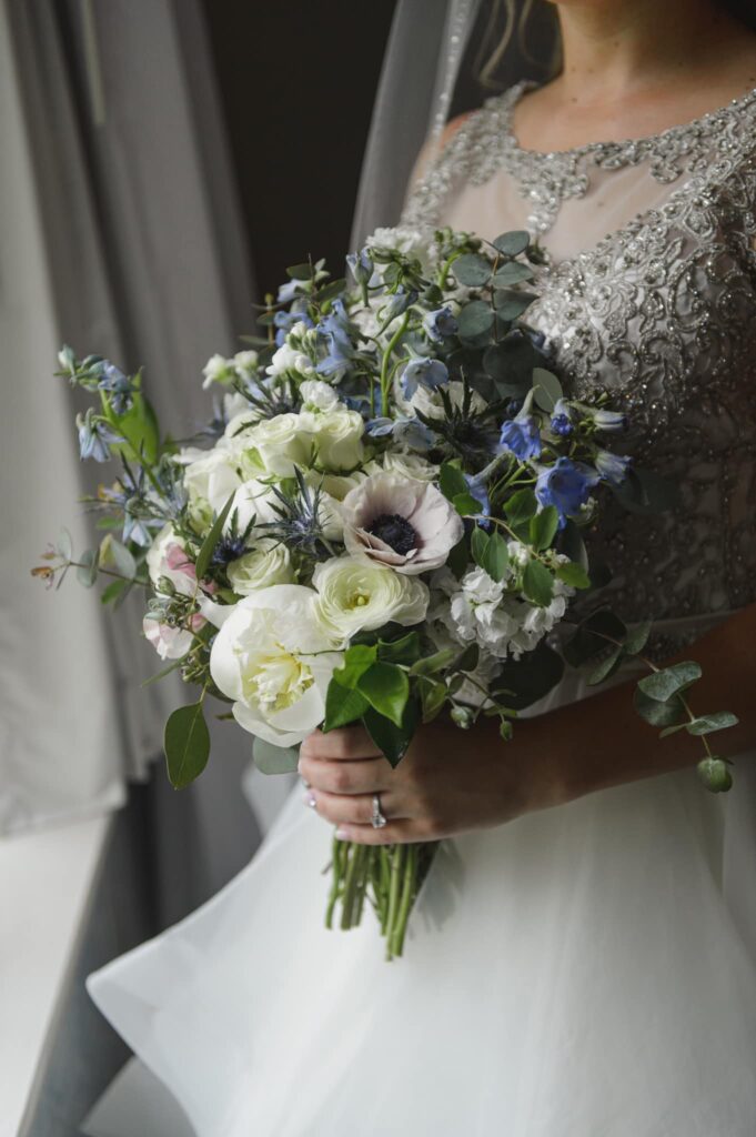 A bride holding a bouquet of white, indigo, and light blue flowers.