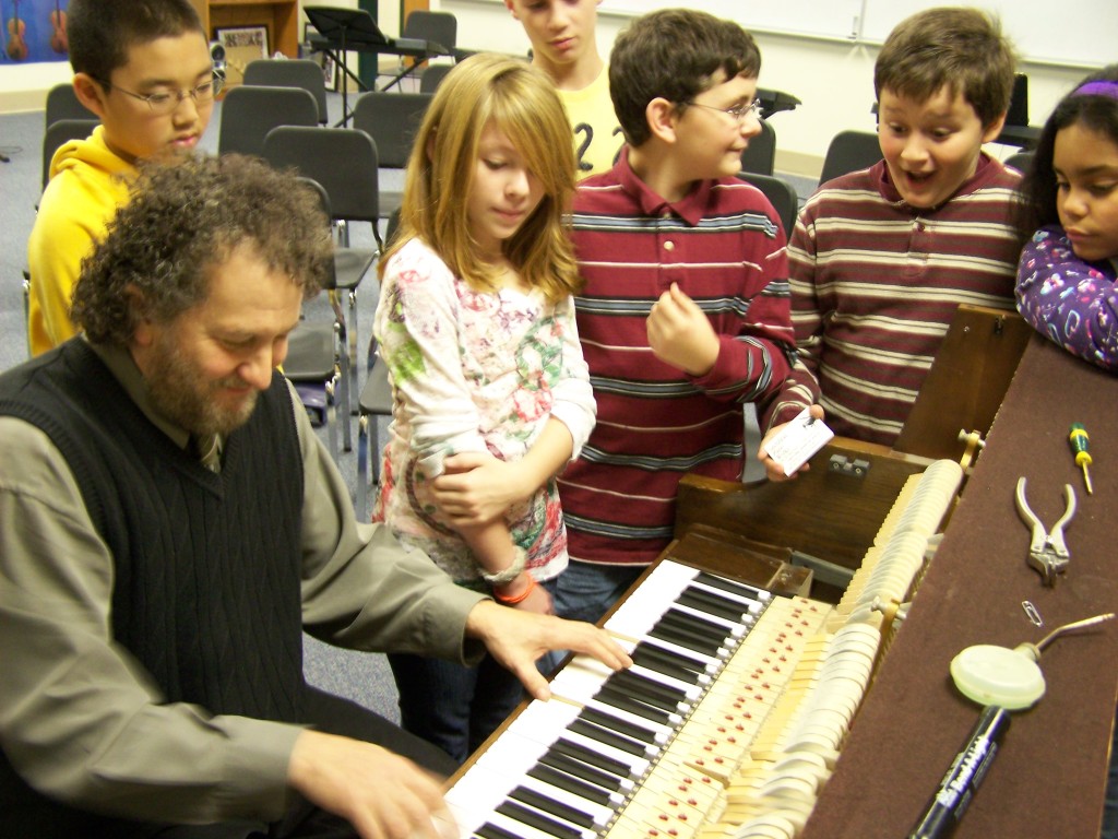 A man tuning a piano in front of children.