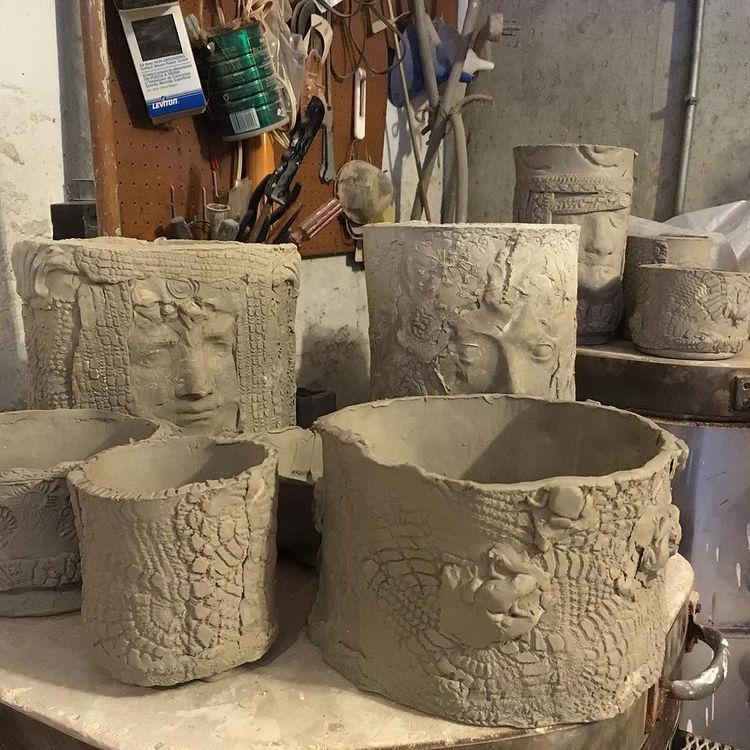 Plain clay pots with faces and textures carved into them.